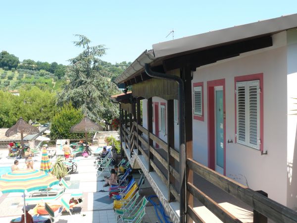 Edifici di villeggiatura con balconi, vista su un'area piscina e colline verdi.