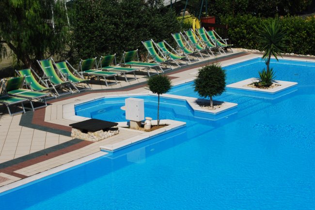 Piscina azzurra con lettini verdi e decorazioni verdi.