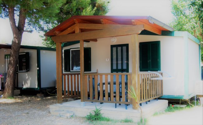 Una casetta con veranda in legno tra gli alberi.