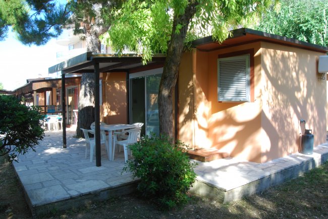 Bungalow con patio e tavolo all'aperto, circondato da alberi.