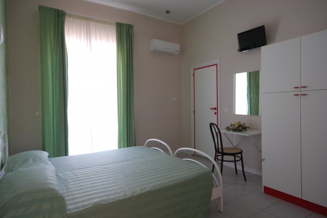 Camera con letto verde e tendaggi coordinati. TV e armadio in un angolo.