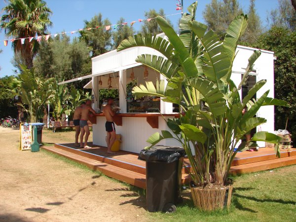 Chiosco bianco circondato da piante tropicali con persone al bancone.