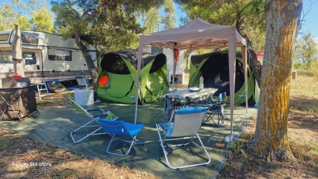 Area campeggio con tende verdi, sedie pieghevoli e tavolo sotto un gazebo.