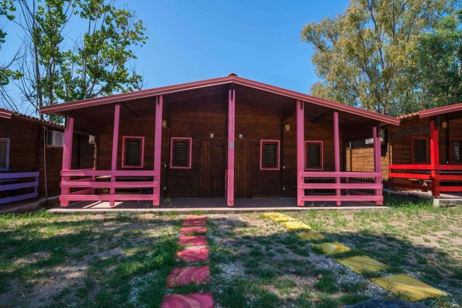 Una casetta di legno con vernice rosa, due porte e un vialetto di pietre colorate.