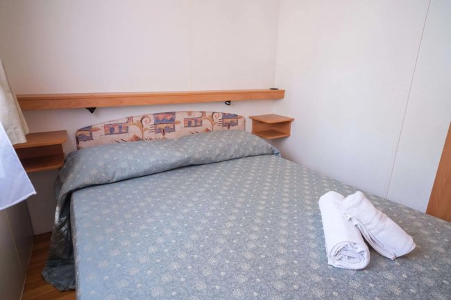 Camera con letto matrimoniale, cuscini e asciugamani bianchi.