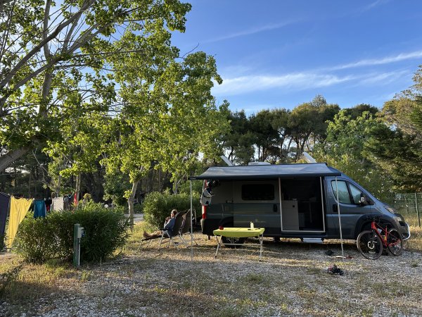 Un camper parcheggiato in una radura, con persone sedute all'esterno.