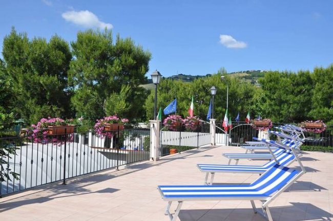 Sdraio blu a righe bianche su una terrazza, alberi e bandiere sullo sfondo.