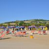 Una spiaggia sabbiosa con lettini e ombrelloni colorati e colline verdi sullo sfondo.