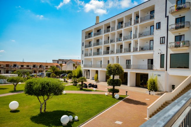 Hotel bianco con balconi, giardino curato e sfere decorative bianche.
