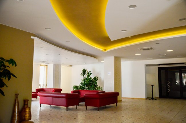 Interno spazioso con soffitto illuminato, divani rossi, piante e decorazioni eleganti.