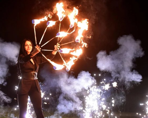 Una donna esegue un'esibizione di giocoleria con fiamme e fuochi d'artificio sullo sfondo.