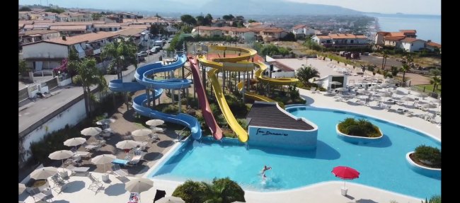Vista aerea di una piscina con scivoli colorati e molte sdraio.