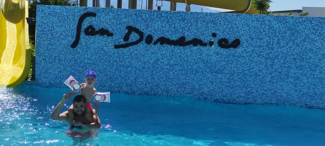 Un adulto e un bambino giocano in piscina davanti a un muro con la scritta 