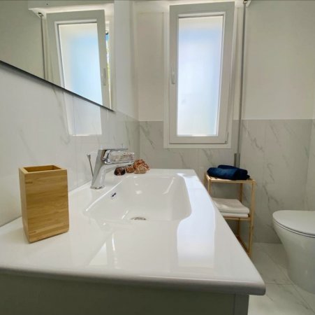 Un moderno bagno bianco con lavabo, finestra e decorazioni in legno.