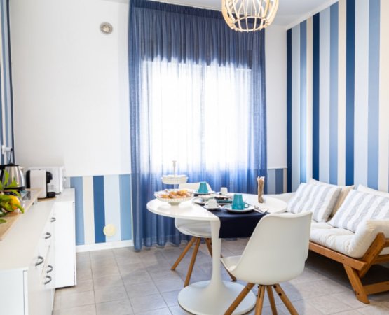 Cucina luminosa con pareti a strisce blu e bianche, tavolo bianco.
