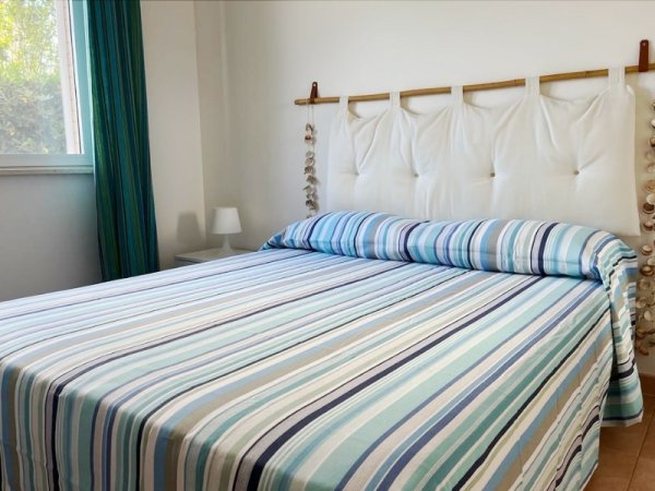 Camera da letto con letto matrimoniale coperto da un copriletto a righe colorate.