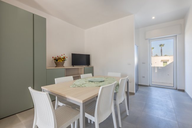 Sala da pranzo con tavolo, TV e porta sul balcone.