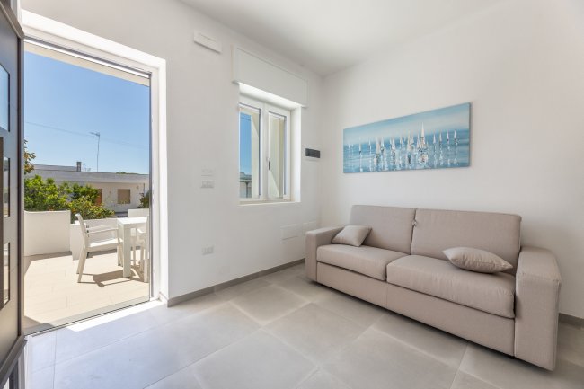 Salotto con divano beige e porta aperta su un terrazzo.