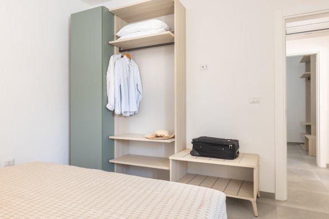 Camera con armadio aperto, camicia appesa e valigia sul tavolo.