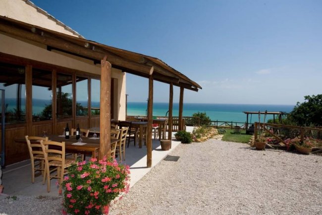 Tavoli all'aperto sotto un portico con vista mare.