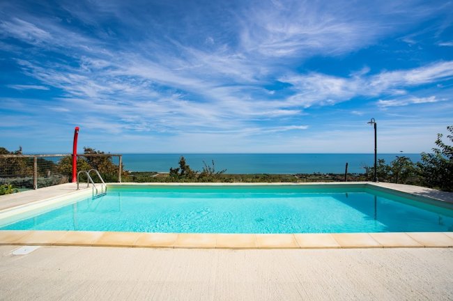 Piscina con vista mare e cielo azzurro con nuvole.