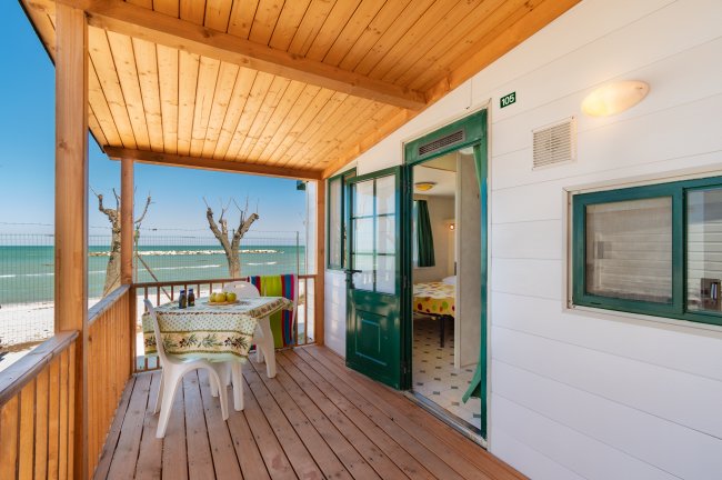 Una veranda con tavolo e sedie, affacciata sul mare, con porta verde aperta.