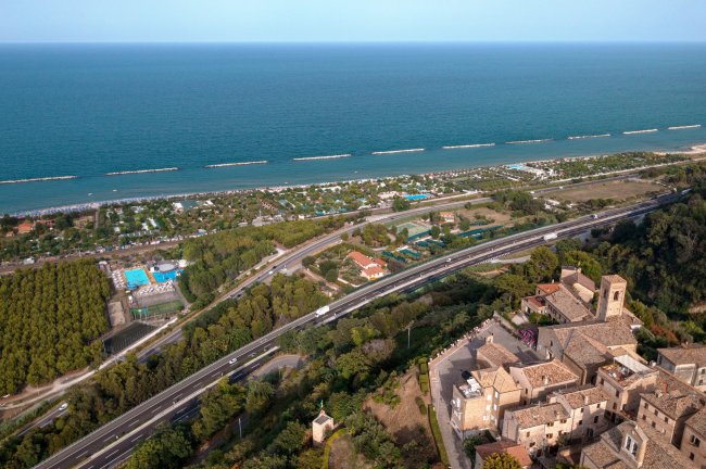 Vista aerea di una località costiera, con autostrada e città storica vicino al mare.