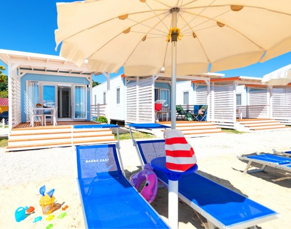 Bungalow sulla spiaggia con lettini blu e ombrellone.