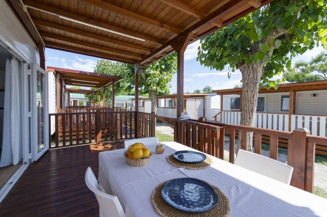 Veranda in legno con tavolo apparecchiato, vista su altre verande, alberi.