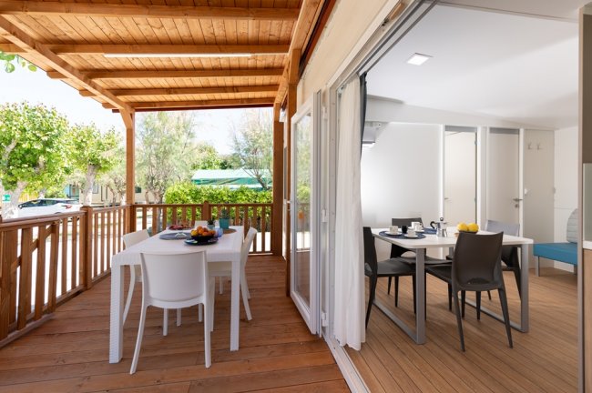 Veranda in legno con tavoli e sedie, affacciata su un giardino verde.