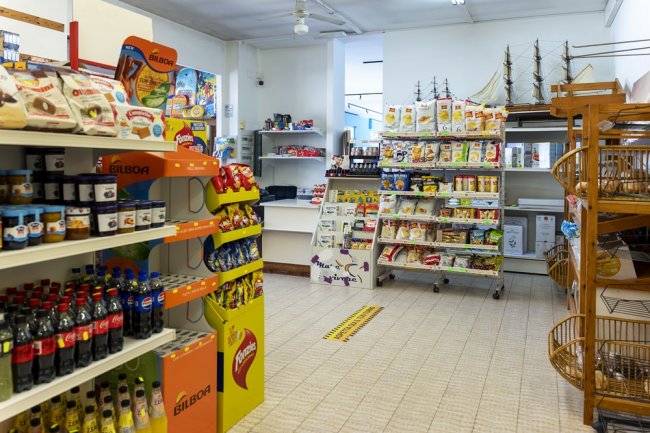 Interno di un minimarket con scaffali pieni di snack e bevande.