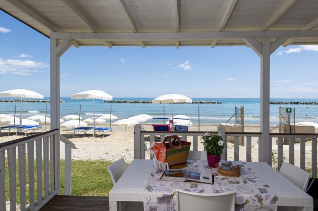 Tavolo all'aperto con vista mare e ombrelloni bianchi in spiaggia.