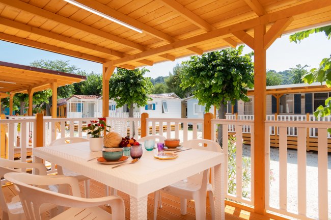Veranda di legno con tavolo apparecchiato e alberi sullo sfondo.