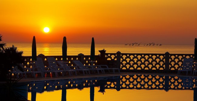 Tramonto sul mare con sedie a sdraio in silhouette.