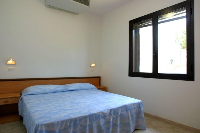 Camera da letto con letto matrimoniale, coperte azzurre, finestra con luce naturale.