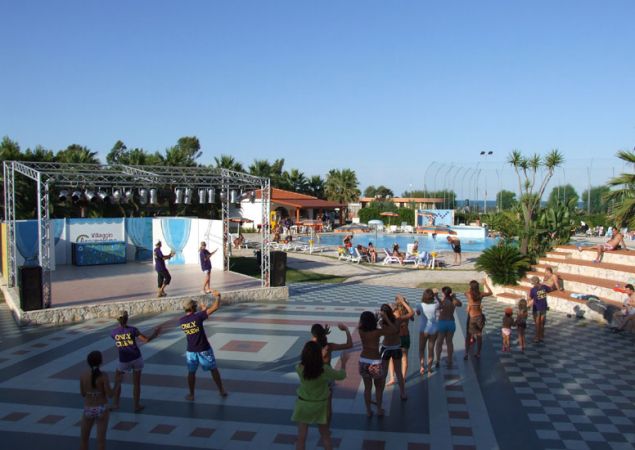 Gruppo di persone segue una lezione di danza all'aperto vicino a una piscina.