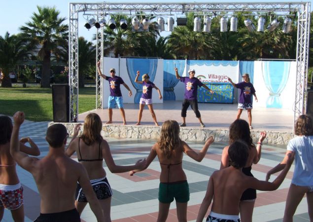 Persone partecipano a una sessione di danza davanti a un palco all'aperto.