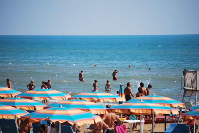 Ombrelloni colorati su una spiaggia, bagnanti in mare azzurro.