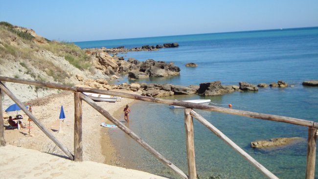 Una spiaggia rocciosa con mare calmo e ombrelloni blu.