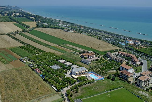 Vista aerea di un paesaggio rurale con campi verdi, edifici e il mare sullo sfondo.
