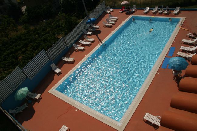 Vista dall'alto di una piscina rettangolare con lettini e ombrelloni intorno.