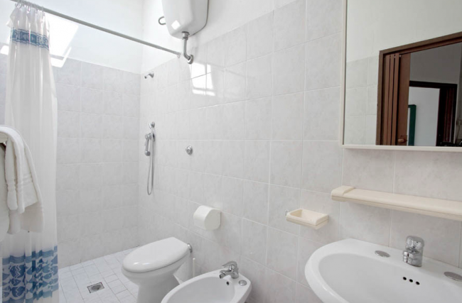Un bagno con doccia, lavabo, water e bidet, interamente piastrellato in bianco.