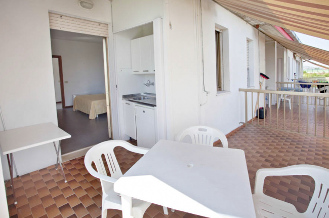 Terrazza con tavolo e sedie bianchi e accesso a una stanza interna.