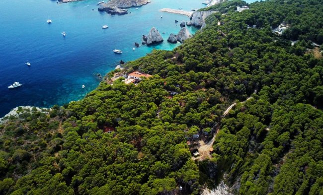 Vista aerea di una costa boscosa con mare blu e barche.