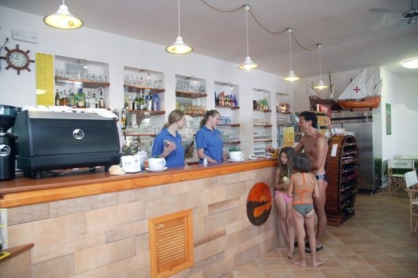 Interno di un bar con due persone dietro il bancone e una famiglia davanti.