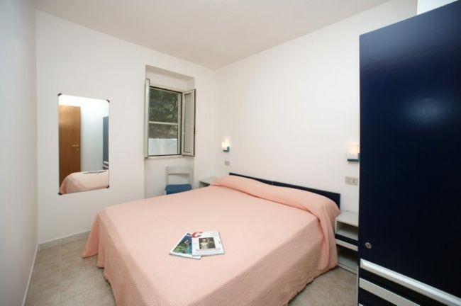 Una camera da letto con letto matrimoniale e copriletto rosa, una finestra aperta e un armadio blu.