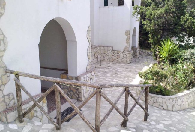 Ingresso con arco e vialetto in pietra, affiancato da piante.