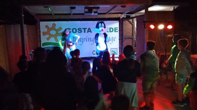 Persone assistono a spettacolo con animatori su palco.