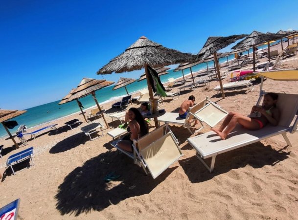 Spiaggia sabbiosa con ombrelloni di paglia e lettini.