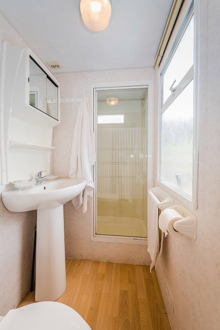 Un bagno con lavabo, specchio, doccia e pavimento in legno chiaro.